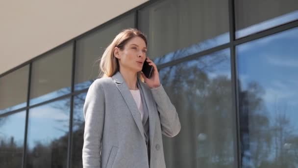 Successful business woman speaking on mobile phone in downtown businesswoman walks down street talking by mobile phone answering business call. Serious female professional having phone conversation. — 비디오