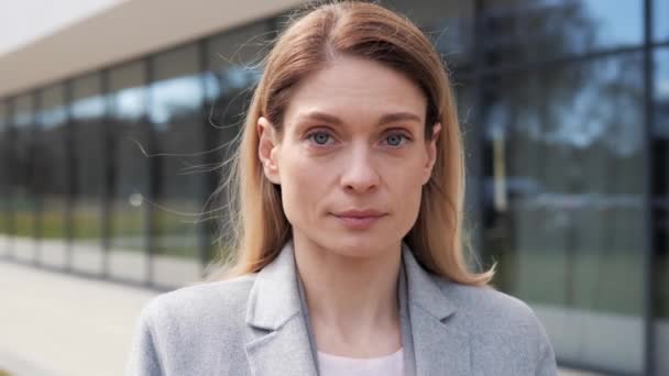 Adult attractive woman looking at camera smiling. Pretty female model posing to camera in front of modern office building outdoors. The girl has a beautiful appearance with healthy white teeth. — Stock Video