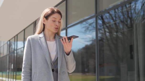 Adult happy businesswoman uses a mobile phone near the business center. Confident businesswoman holding smartphone recording voice message or activating digital assistant making business call. — Stock Video