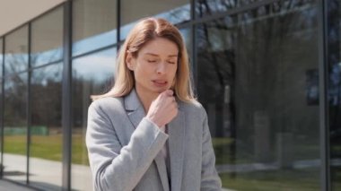 Yetişkin Hastalıklı İş Kadını dışarıda dikilirken resmi bir takım elbise giyip öksürüyor. Güzel olmayan beyaz bir kadının göğüs ağrısı çeken öksürüğünün portresi. Enfeksiyon ve virüs. Sağlık kavramı.