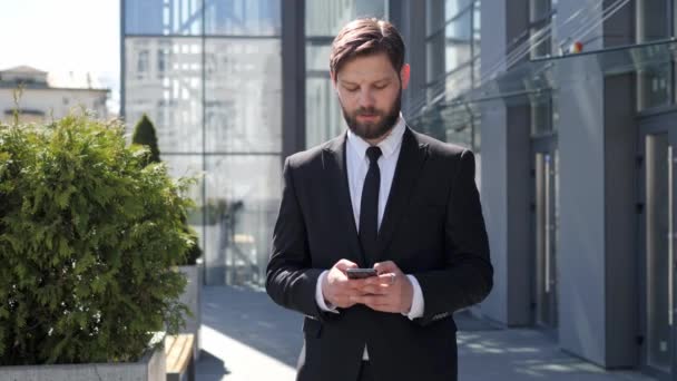 Successful happy Bearded Businessman is texting Messages answer e-mail on his modern Smartphone. Young Man is standing in Business Quartal, having good Mood, looking Satisfied. Successful Lifestyle. — стоковое видео