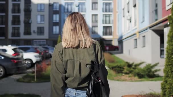 Hermosa mujer rubia caminando por la ciudad. Divertida joven feliz en gafas de sol agitar la cabeza para hacer volar el pelo. Atractiva joven dama se da la vuelta y mira a la cámara al aire libre. — Vídeo de stock