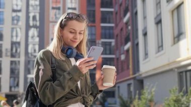 Portrait of a Cheerful Caucasian Female Wearing Smart Casual Clothes and Using Smartphone on the Urban Street. Girl in Big City Connecting with People Online, Messaging and Browsing Internet.