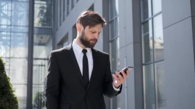 Yakışıklı, kravatlı genç bir iş adamı. Akıllı telefon mesajları kullanıyor. Sokakta mesajlar okuyor. İş stili dinleme ve cep telefonunda kaydırma yapan erkek model. Açık havada. Başarılı insanlar..