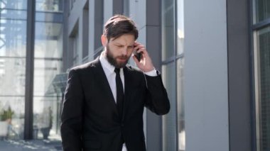 Hipster young smart businessman talking in telephone in city. The man wearing stylish suit walking to working having phone call outdoor. Telecommunication and mobile network for business concept.