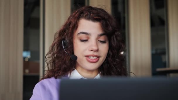 Närbild av vackra kvinna bär headset använda laptop gör videokall talar med kunden sitter distanserat i kontorsrummet. Kvinnlig student njuter av lärande med online lärare videokonferens händelse . — Stockvideo