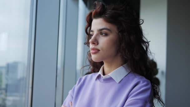 Young business thoughtful woman freelancer thinking near the window. Pretty girl with deep brown eyes standing in office near panoramic window with a city landscape. The talented designer is inspired. — Stockvideo