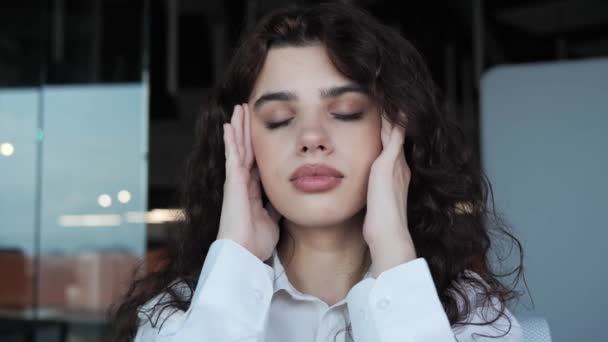 The office worker is having headache. Closeup exhausted overworked young pretty woman massaging temples. Stressed unhealthy girl standing in office feeling tired suffering from migraine, panic attack. — Stock video