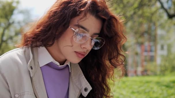 Beautiful thoughtful girl with curly hair making notes in notebook. Close up face of female designer enjoying nature standing near beautiful tree in spring. Remote work student Lifestyle Concept. — Video Stock