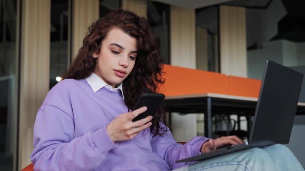 Χαμογελαστός νεαρός επαγγελματίας επιχειρηματίας που χρησιμοποιεί το κινητό τηλέφωνο που εργάζονται σε φορητό υπολογιστή κάθεται σε άνετη καρέκλα δακτυλογράφηση μήνυμα. Γυναίκα πελάτης κάνει επιβεβαίωση online ιστοσελίδα παραγγελία παράδοση έννοια. — Αρχείο Βίντεο