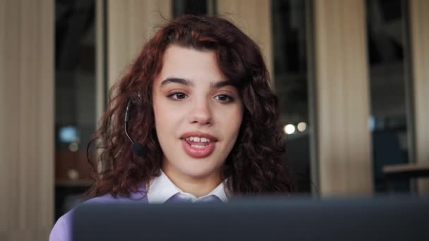 Sonriendo hermosa mujer usa auriculares portátil hacer videocall hablando con el cliente se sienta a distancia en la habitación de la oficina. Estudiante disfruta de aprender con el evento de videoconferencia profesor en línea indoor. — Vídeo de stock