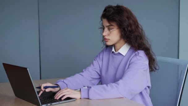 Creative pretty manager with curly hair wearing in violet sweater, writes in notepad, works on modern laptop computer, uses organizer app, sits in office . Experienced entrepreneur, working concept. — стоковое видео