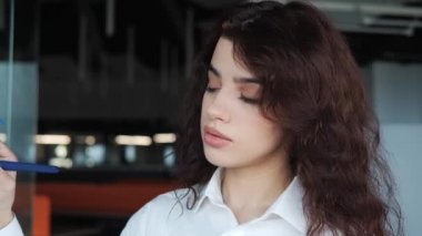 Modern işyerindeki cam levhalara beyaz tişörtlü, akıllı bir ofis çalışanı etiketler yazıyor. Kapalı alanda uygun bir çözüm arayan konsantre bir kadın. Güzel kız faiziyle çalışıyor..