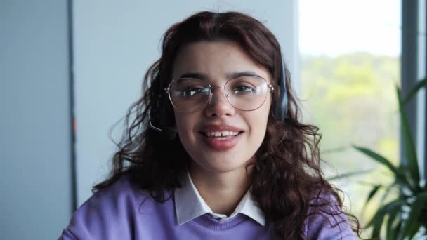 Attractive teacher wears headphones and glasses, studies online with an Internet, learns a language, talks, looks at a laptop, focuses on video calls, distance job, learning concept. — Vídeo de Stock