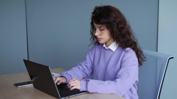 Portrait of beautiful female it software worker with curly hair and glasses in office. Attractive girl look at the screen of laptop typing program code. Young business woman chatting online indoor. — Stock video