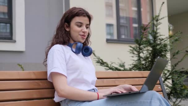 Young pretty girl freelancer talking using webcam on laptop outdoors speaking into camera at remote interview female student makes conference communicates online in internet video chat outside. — ストック動画