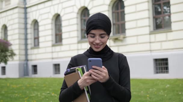 Young arabian asian muslim student woman in hijab holding using mobile smartphone typing browsing chatting with friends browsing social media internet near university islam religious education concept — Vídeo de Stock