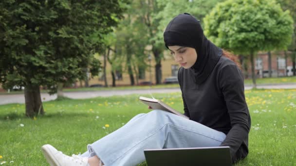 Mujer musulmana confiada islámica estudiante en hijab sentado en el césped césped en el parque al aire libre maestra en línea mentor preparándose para la conferencia usando computadora portátil comunicación en línea distante. — Vídeo de stock