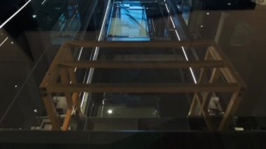 Cinematic shot of modern glass elevator with group of businessmen move up. Successful people take the lift to the top of Business Center. Stylish man and Woman talking while using smartphone.