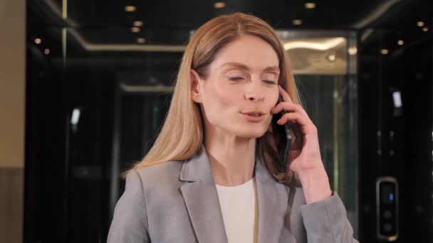Closeup face woman positive business lady talking on smartphone in hallway. Smiling businesswoman calling by mobile phone in corridor. Portrait of friendly blonde female ceo indoor. — Αρχείο Βίντεο