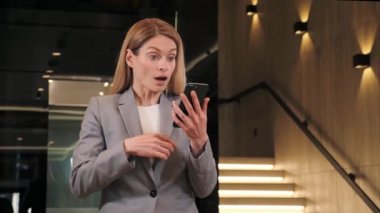 Mutlu iş kadınının portresi asansörün yanındaki modern ofis salonunda cep telefonunda başarıdan zevk alıyor. Kapalı kapılar ardında neşeli bir kız telefonda iyi haberler okuyor. Şaşkın kadın telefonda zaferi kutluyor..