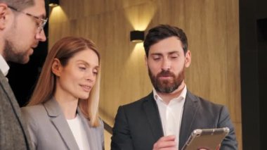 İşadamı tablet bilgisayarda proje gösteriyor. Yönetici takım çalışanları, CEO 'nun görüşmelerini dinliyorlar. Koridorda sonuçları tartışıyorlar. Şık şirket liderleri yönetici danışmanı içeride konuşuyor..