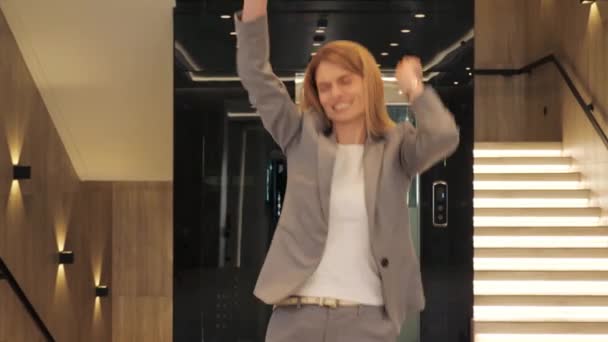 Feliz mujer de negocios emocionada celebrando la victoria, bailando en la oficina del vestíbulo moderno. Mujer divirtiéndose disfrutar de oportunidades de trabajo. Gente de carrera. Celebración. Mujer celebra exitoso proyecto de comercio electrónico. — Vídeo de stock