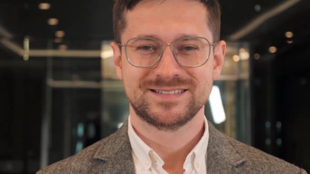 Portrait of Smart Bearded Handsome IT Specialist Wearing Glasses Charmingly Smiles Looking at Camera. Positive face of businessman standing in modern office indoor. Close up male facial expression. — Stockvideo