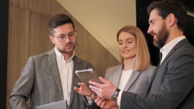 Etkili iş adamı tablet bilgisayarda proje gösteriyor. Yönetici takım çalışanları CEO 'nun müzakerelerini dinliyor ve sonuçları koridorda tartışıyorlar. Şık şirket liderleri yönetici danışmanı içeride konuşuyor..