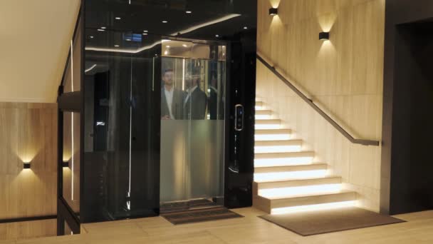 Group of businessmen are moving up in a modern glass elevator. Successful people take the lift to the top of Business Center. Stylish man and woman talking discuss the project inside lift. — Αρχείο Βίντεο