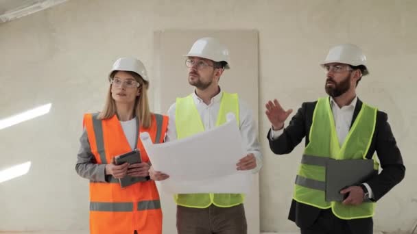 Group of businesspeople and engineer inspecting real estate. Investor, architect, engineer analyzing and discuss the plan of construction site wearing a safety helmets. Finish Industrial Building. — Αρχείο Βίντεο