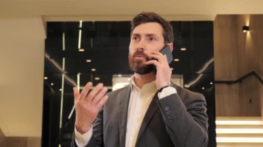 Portre yakışıklı adam iş merkezinde telefon görüşmesi yapıyor. Modern cam asansörün yanındaki koridorda akıllı telefondan konuşan bir iş adamı. İçeriden telefon var. Modern aygıt kullanan bir ofis çalışanı.