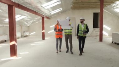 Yapının bir planını elinde tutan mühendis teknisyen, yatırımcılara kira alışverişi için inşaat nesnesini teftiş ediyor. İnşaat alanı uzmanları siteyi inceliyor.