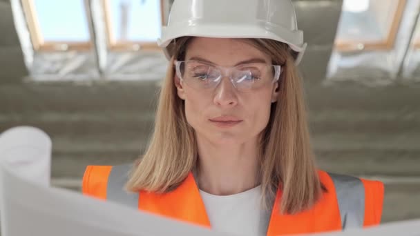 Portrait of focused talented pretty female architect analyzing blueprint in modern new building standing near window sincerely looking at camera. Busy concentrated professional adult woman. — Vídeo de Stock