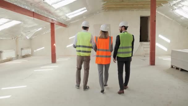 Group of three people two businessman investor and architect engineer analyzing and discuss the plan of construction site they wearing a safety helmets. Investor and Worker Finish Industrial Building. — Stockvideo