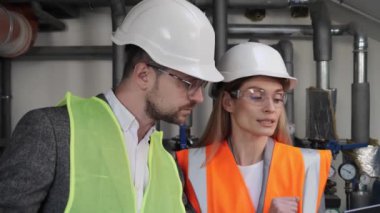 Güvenli Üniforma Giyen ve Bilgisayarda Çalışan İki Farklı Profesyonel Endüstri Mühendisi. Teknisyen ve kadın işçiler kazan dairesinde toplantı yapıyorlar..