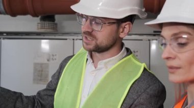 Güvenlik Üniforması Giyen ve Laptop Bilgisayar Kullanarak Çalışan İki Farklı Profesyonel Endüstri Mühendisi. Teknisyen ve Kadın İşçi Kazan dairesinde Bir Toplantıda Konuşuyor.