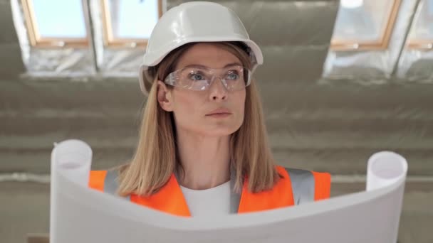 Portrait of thoughtful talented pretty female architect analyzing blueprint in modern building standing at window. Busy concentrated adult woman looking at architectural plan thinking. Talent concept. — Wideo stockowe
