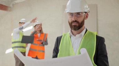 İnşaat tarafında duran koruyucu kasklı ve gözlüklü bir mühendisin portresi. Erkek ve kadın mühendisler dizüstü bilgisayarlarını tutarak yeni emlak projesini tartışıyorlar.. 