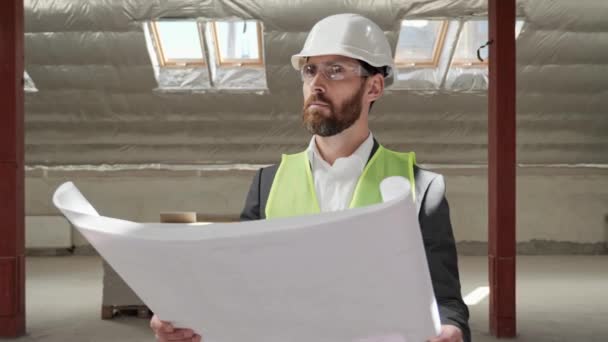 Thoughtful professional handsome engineer architect examining blueprint in empty real estate. Portrait of serious male expert in helmet thinking planning construction building project. Engineering. — Vídeos de Stock
