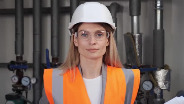 微笑富有创造力的女工程师。在暖气室穿着制服、眼镜和硬帽衫的专业工业工程师的肖像。美丽的专业人员常设生产室. — 图库视频影像