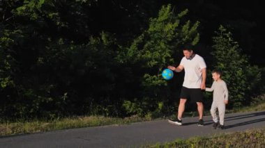 Beyaz tişörtlü Asyalı adam gün batımında antrenmana gitmek için bebek elini tutuyor. Spor, sağlıklı aile. İçtenlikle gülümseyen küçük çocuk olumlu duygular yaşıyor. Çinli bir erkek çocukla yürüyor.