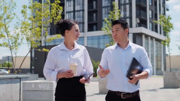 ビジネス街を歩くビジネスマンのエグゼクティブチーム 多民族の専門家の従業員の経営者は屋外でプロジェクトの結果を議論する ビジネスウーマンとアジアの男が話してる — ストック動画