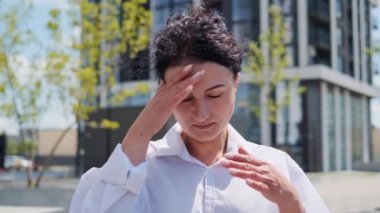 Yorgun, genç, yetişkin bir iş kadını, dışarıda baş ağrısı çeken bir ofis çalışanı. Stresli kadın masaj kafası. Korkunç bir acı çeken kadın, migren ağrısı, hava değişimi.