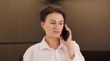 Yakın plan, ofisin içinde akıllı telefondan konuşan kendine güvenen bir iş kadını. Yetişkin bir iş kadını koridorda cep telefonunu arıyor. İş merkezi koridorunda duran şık bir bayanın portresi.