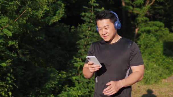 Korean Sportsman Wireless Headphones Holding Mobile Phone Listening Music Χρησιμοποιώντας — Αρχείο Βίντεο