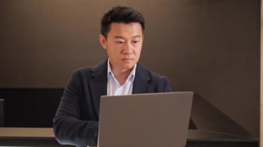 Kendine güvenen Çinli iş adamı iş yerinde dizüstü bilgisayar kullanıyor, erkek yönetici lobideki bilgisayarlarda iş e-postası yazıyor, internette sörf yapıyor, online ofis işi yapıyor.