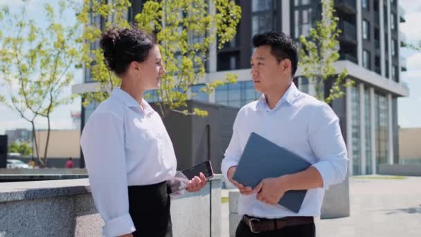 オフィスビルの近くに立っているアジア民族のビジネスマンは かなりスタイリッシュな女性とのコラボレーションプロジェクトを議論する 中国人男性保持ラップトップ話とともに女性同僚屋外 — ストック動画