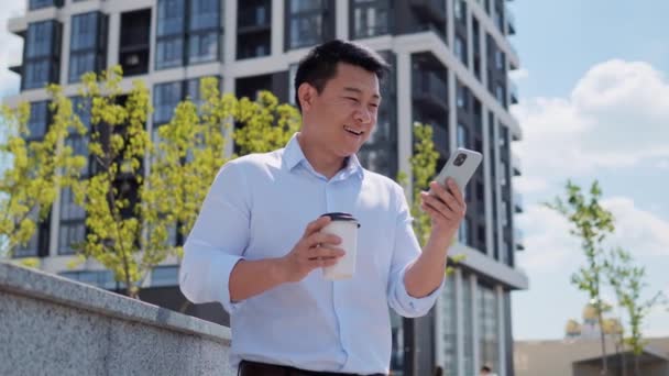 Exted Przystojny Biznesmen Azjatycki Patrząc Smartphone Picie Kawy Świeżym Powietrzu — Wideo stockowe