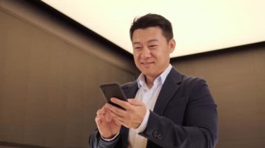 Modern ışık ofisinde cep telefonu uygulaması kullanan kendine güvenen Koreli bir adam. Pozitif Asyalı iş adamı finans haberlerine bakıyor, gülümsüyor ve iyi haberleri evde okuyor. Başarılı Çinli yetişkin erkek.